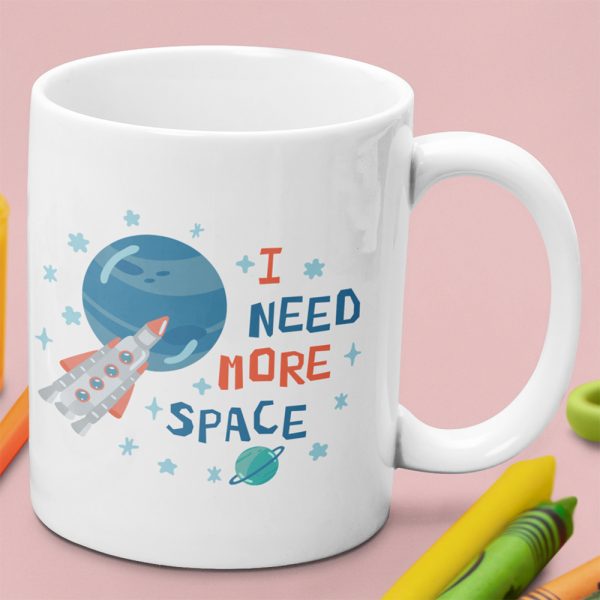 A close up of a kids mug with the words I need more space printed on it alone with planets stars and moons