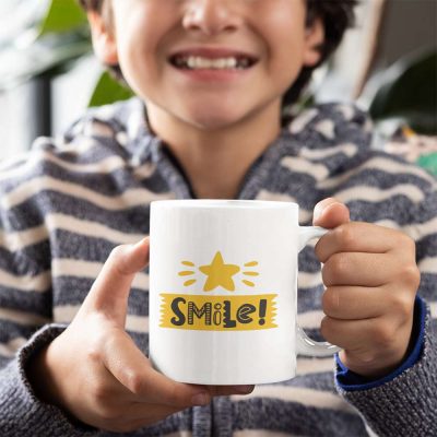 A photograph of a young boy with a mug with a bright yellow star and the colourful words smile printed on it