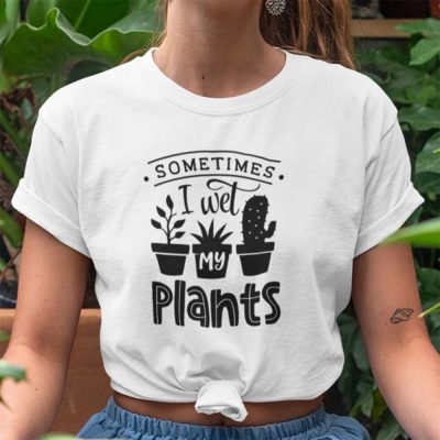 A close up of a lady surrounded by plants in a yoga pose wearing a white t shirt with the words Sometimes I Wet My Plants printed on it along with images of potted plants