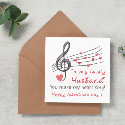 a square white card on top of a kraft coloured envelope. The card has an image of a musical treble clef with love hearts instead of musical notes on a music sheet. the words read, Husband, you make my heart sing, happy valentine's day